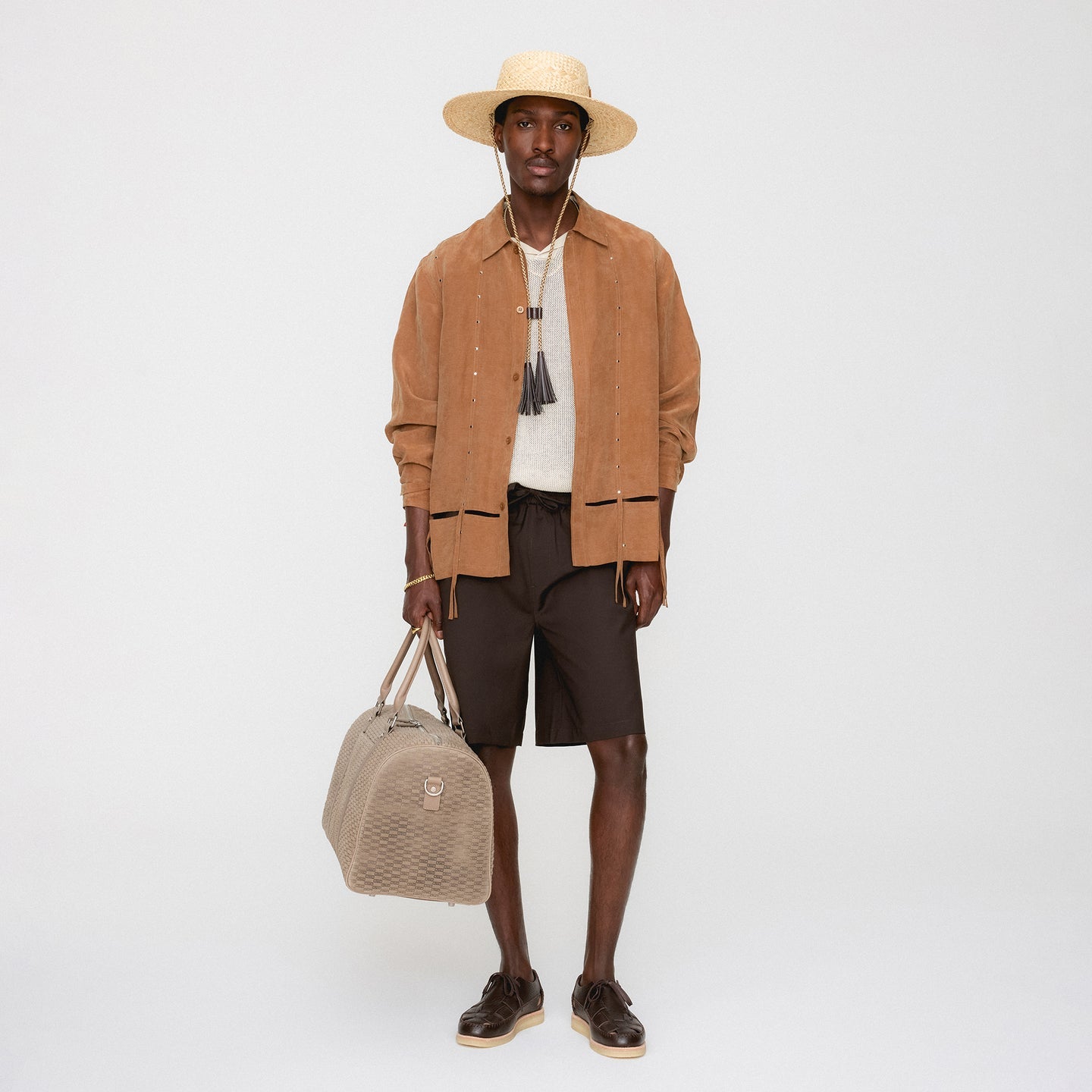Man wearing a brown jacket, hat, and holding a beige bag on a white background